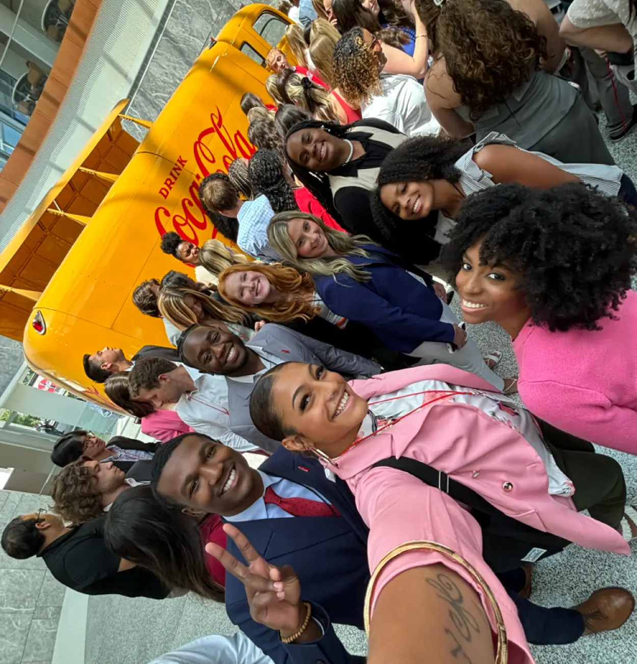 Group of students and staff posing together next to a vintage yellow Coca-Cola-branded bus