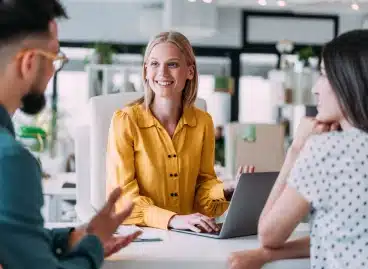 Team member presenting a laptop screen to two colleagues at a desk